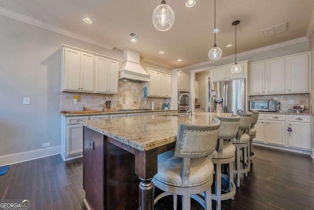 kitchen with decorative light fixtures, white cabinetry, custom exhaust hood, stainless steel appliances, and a center island with sink