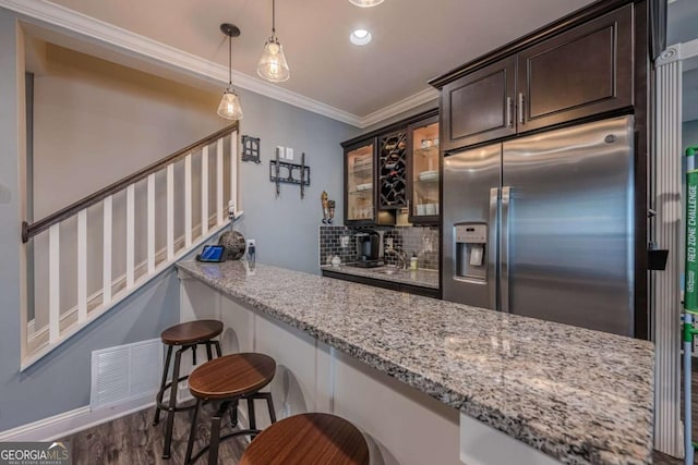 kitchen featuring stainless steel refrigerator with ice dispenser, dark brown cabinets, ornamental molding, a kitchen breakfast bar, and light stone countertops