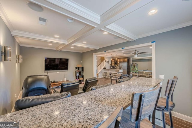 kitchen featuring hardwood / wood-style flooring, beam ceiling, light stone counters, coffered ceiling, and a kitchen bar