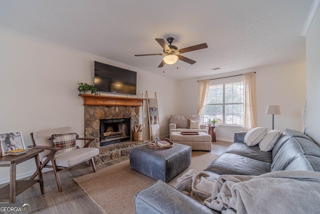 living room with crown molding, a stone fireplace, a textured ceiling, and light wood-type flooring