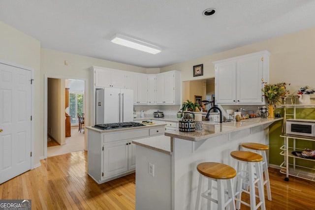 kitchen featuring white appliances, a kitchen bar, kitchen peninsula, and white cabinets