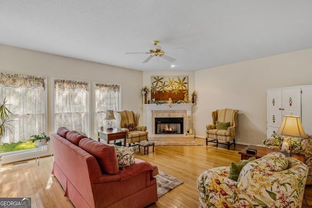 living room with a fireplace, ceiling fan, and light wood-type flooring