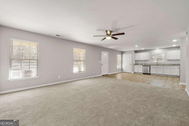 unfurnished living room with ceiling fan, light colored carpet, plenty of natural light, and sink