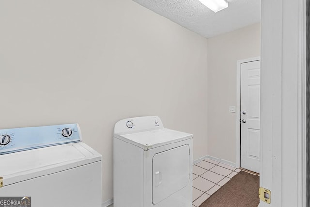 clothes washing area with washer and clothes dryer, a textured ceiling, and light tile patterned flooring