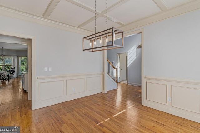 unfurnished dining area with ornamental molding, wood-type flooring, coffered ceiling, and a chandelier