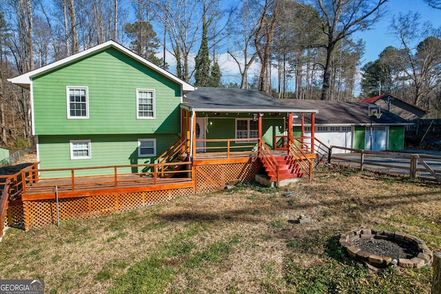 rear view of property featuring a garage, a yard, covered porch, and a fire pit