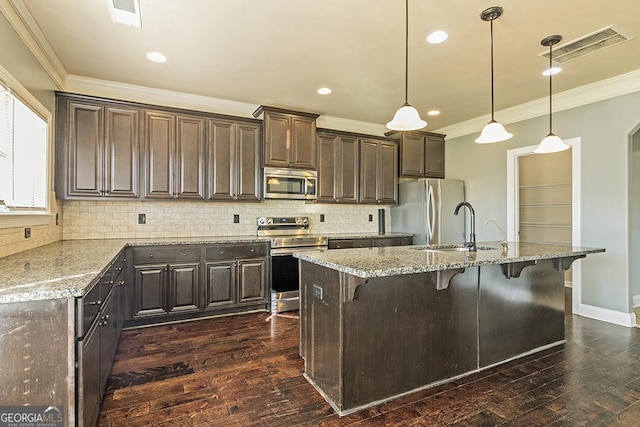 kitchen featuring crown molding, appliances with stainless steel finishes, light stone counters, an island with sink, and decorative light fixtures