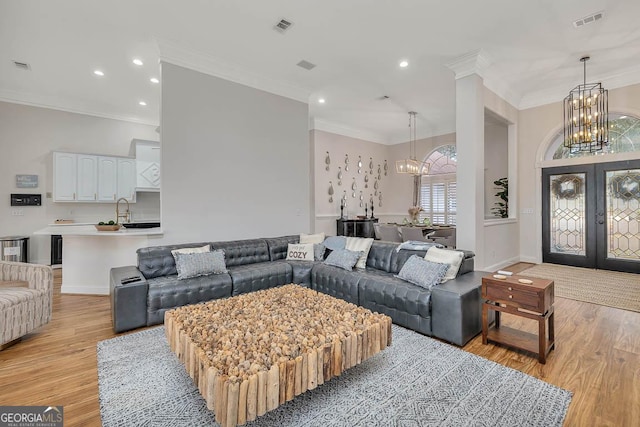 living area with visible vents, ornamental molding, french doors, light wood-style floors, and a notable chandelier