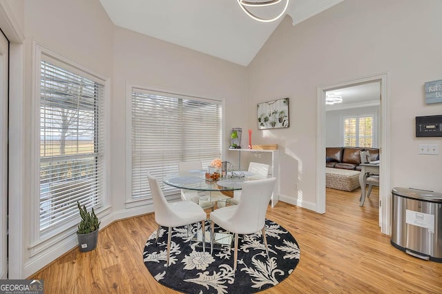 dining area with high vaulted ceiling, light wood-style flooring, and baseboards