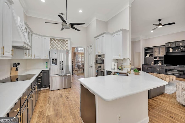 kitchen featuring white cabinets, custom range hood, appliances with stainless steel finishes, light wood-style floors, and a sink