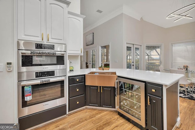 kitchen featuring beverage cooler, double oven, a peninsula, and white cabinetry