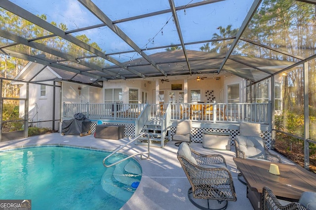 outdoor pool featuring a deck, glass enclosure, ceiling fan, and a patio area