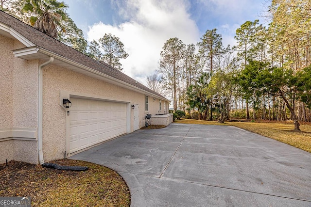 view of side of property featuring an attached garage, driveway, and stucco siding