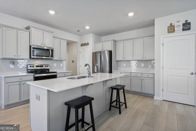 kitchen with sink, gray cabinets, a center island with sink, stainless steel appliances, and a kitchen bar