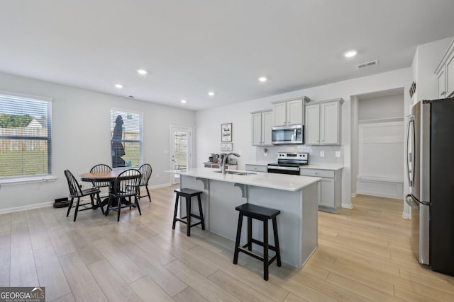 kitchen with appliances with stainless steel finishes, a breakfast bar, sink, a kitchen island with sink, and light wood-type flooring