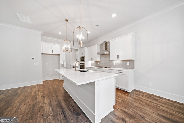 kitchen with appliances with stainless steel finishes, a sink, ornamental molding, wall chimney exhaust hood, and an island with sink