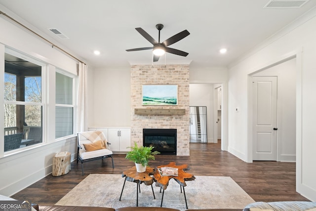 living room with visible vents, a brick fireplace, crown molding, baseboards, and wood finished floors