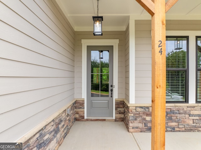 doorway to property with roof with shingles, covered porch, and stone siding