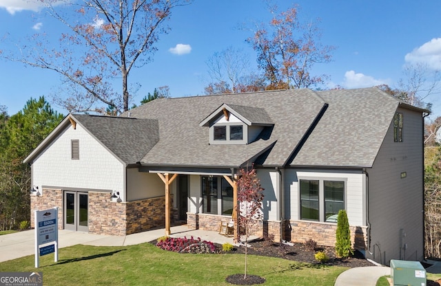 view of front of house with stone siding, concrete driveway, a front yard, and roof with shingles