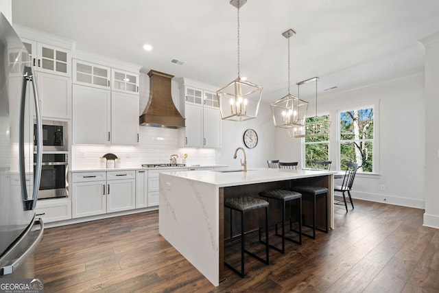 kitchen featuring dark wood-style flooring, a sink, custom range hood, appliances with stainless steel finishes, and tasteful backsplash