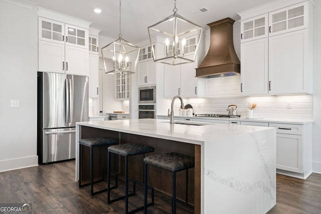 kitchen with premium range hood, a kitchen island with sink, tasteful backsplash, appliances with stainless steel finishes, and dark wood-style flooring