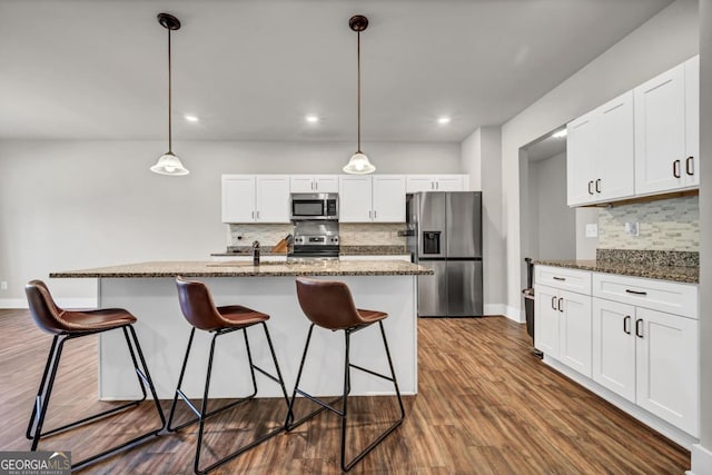 kitchen with pendant lighting, white cabinets, appliances with stainless steel finishes, and dark stone countertops