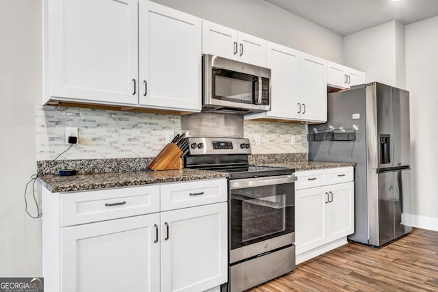 kitchen with white cabinetry, stainless steel appliances, light wood-type flooring, and dark stone countertops