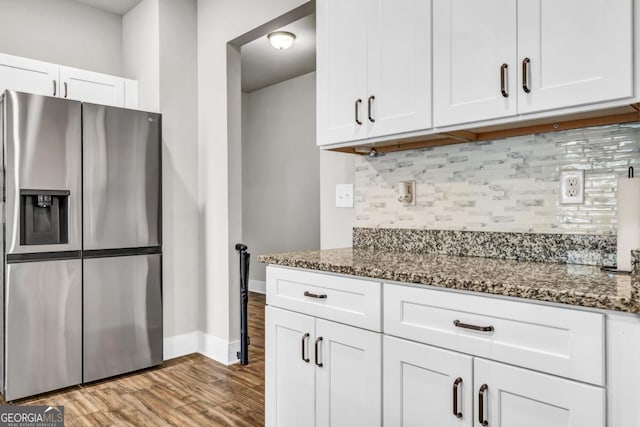 kitchen with light hardwood / wood-style flooring, white cabinetry, stainless steel refrigerator with ice dispenser, tasteful backsplash, and dark stone counters