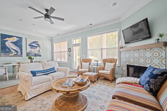 living room with a tiled fireplace, hardwood / wood-style floors, ornamental molding, and ceiling fan