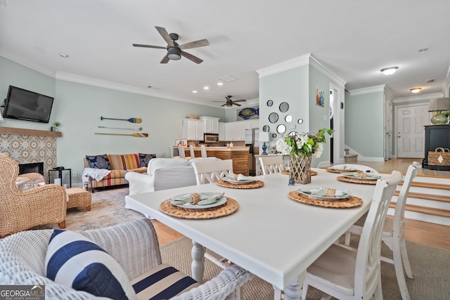 dining area with crown molding, a fireplace, ceiling fan, and light wood-type flooring