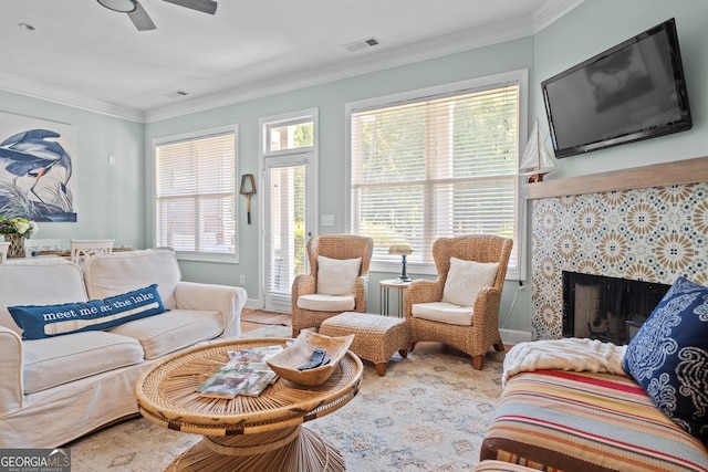 living room with crown molding, ceiling fan, a healthy amount of sunlight, and a tiled fireplace