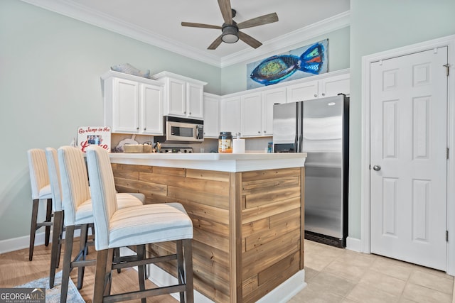 kitchen featuring light tile patterned flooring, white cabinets, ceiling fan, stainless steel appliances, and crown molding