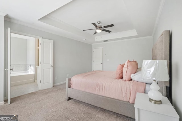 carpeted bedroom with a tray ceiling, ornamental molding, ceiling fan, and ensuite bathroom