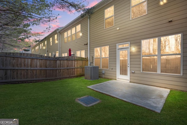 back house at dusk featuring cooling unit, a patio area, and a lawn