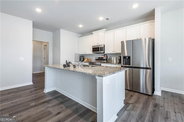 kitchen with dark wood-type flooring, appliances with stainless steel finishes, a kitchen island with sink, white cabinetry, and light stone countertops