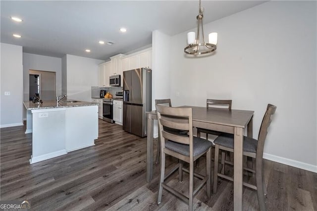 kitchen featuring appliances with stainless steel finishes, decorative light fixtures, white cabinetry, dark hardwood / wood-style flooring, and light stone countertops