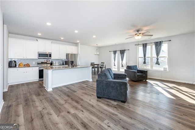 kitchen with an island with sink, white cabinetry, hardwood / wood-style flooring, light stone counters, and stainless steel appliances