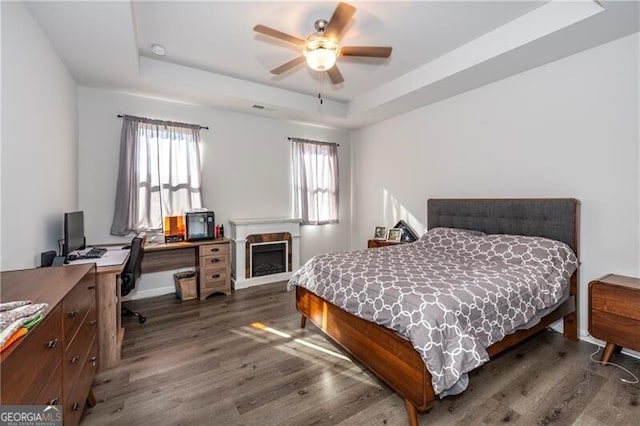 bedroom featuring a raised ceiling, dark wood-type flooring, and ceiling fan