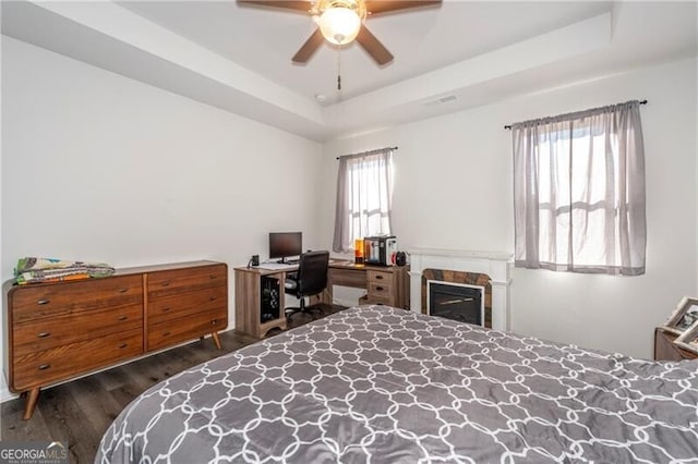 bedroom with ceiling fan, dark hardwood / wood-style flooring, and a tray ceiling