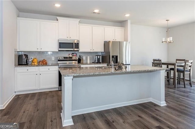 kitchen with white cabinetry, a kitchen island with sink, stainless steel appliances, dark hardwood / wood-style flooring, and decorative light fixtures