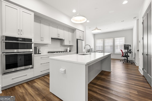 kitchen with sink, hanging light fixtures, stainless steel appliances, white cabinets, and a center island with sink