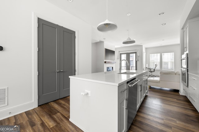 kitchen with sink, a kitchen island with sink, stainless steel appliances, dark hardwood / wood-style flooring, and decorative light fixtures