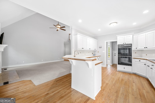 kitchen featuring a breakfast bar, white cabinetry, kitchen peninsula, double oven, and ceiling fan