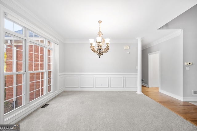 carpeted empty room with an inviting chandelier, ornamental molding, and ornate columns