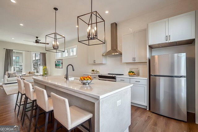 kitchen featuring appliances with stainless steel finishes, white cabinets, a kitchen island with sink, dark wood-type flooring, and wall chimney range hood