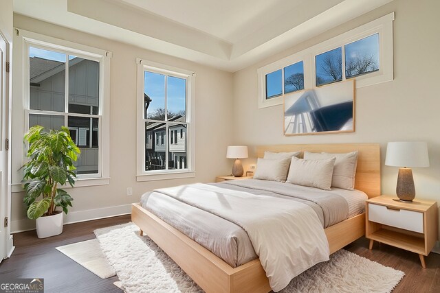 bedroom with multiple windows, dark hardwood / wood-style flooring, and a tray ceiling