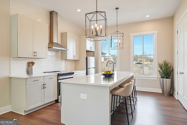 kitchen with refrigerator, sink, wall chimney exhaust hood, a center island with sink, and electric stove