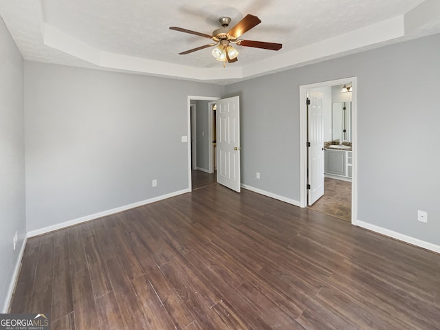 unfurnished bedroom with ceiling fan, dark wood-type flooring, a raised ceiling, and a textured ceiling