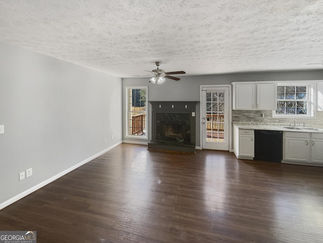 unfurnished living room featuring sink, ceiling fan, a fireplace, a textured ceiling, and dark hardwood / wood-style flooring