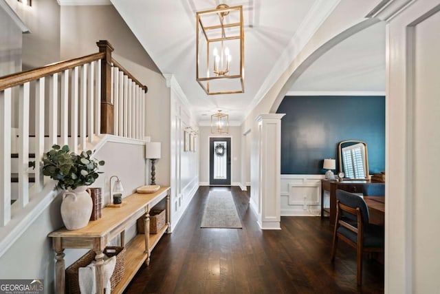 foyer entrance featuring an inviting chandelier, ornamental molding, dark hardwood / wood-style flooring, and decorative columns